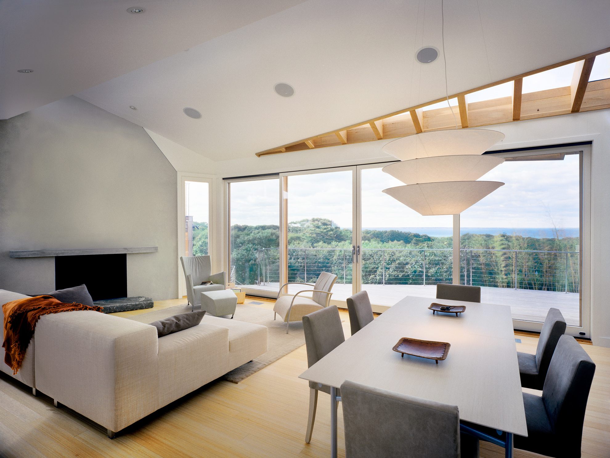 Living and dining room interior with white furniture and a white concrete chimney opens to views to views of ocean beyond through a wall of large glass patio doors.