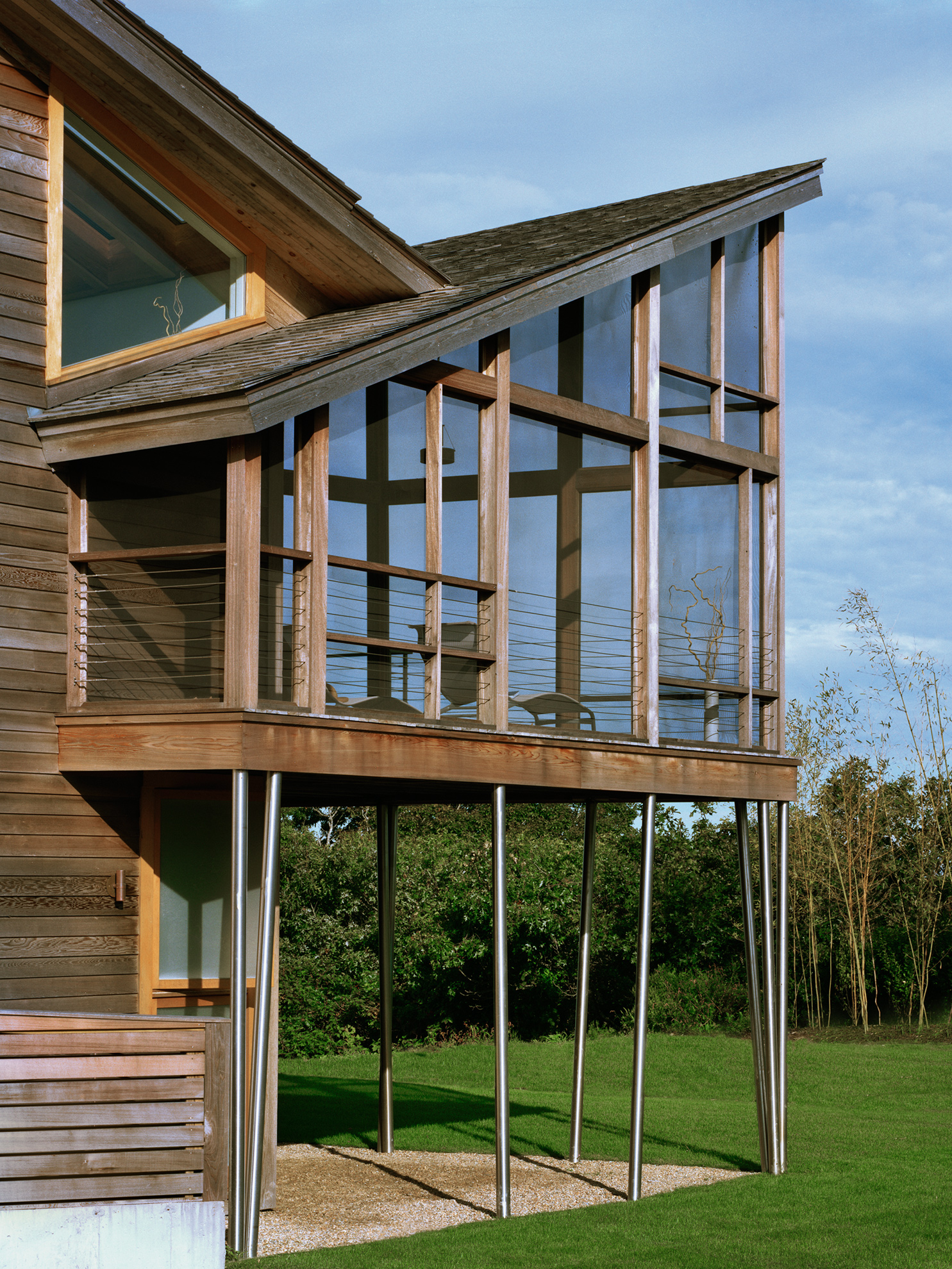 Enclosed back porch  framed in cedar has a cedar roof that tilts up toward the backyard. 
                                                                                It sits on a deck above the first floor that is supported by thin, round metal columns which angle slightly in various directions.