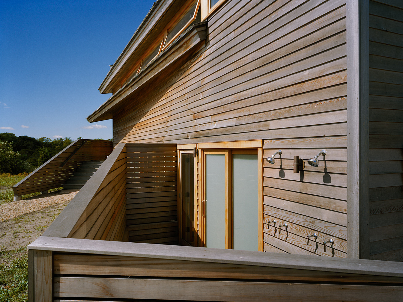 Horizontal cedar slat angled walls surround an outdoor shower at the end of the house.
