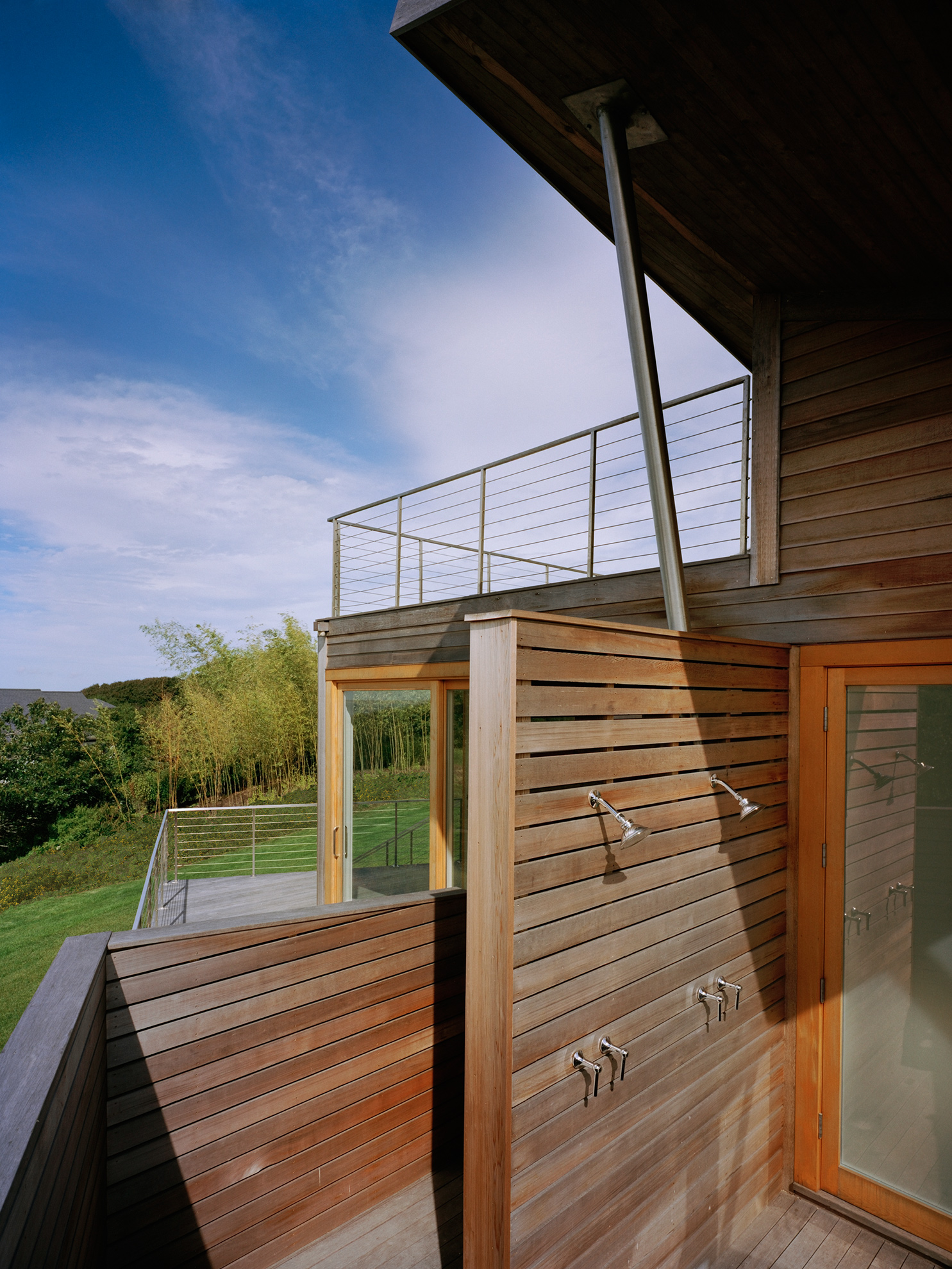 Close up view of outdoor shower area, defined by walls sloping down surrounding it, everything clad in new cedar siding.