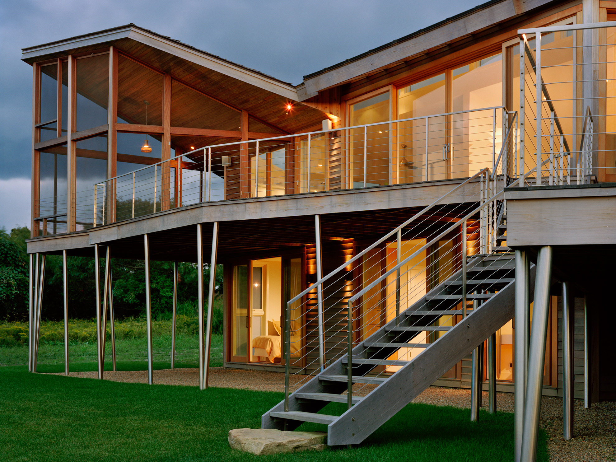 Back of house view zoomed in on screened porch with angled roof pointing up and wood deck and stairs coming down from the second floor.