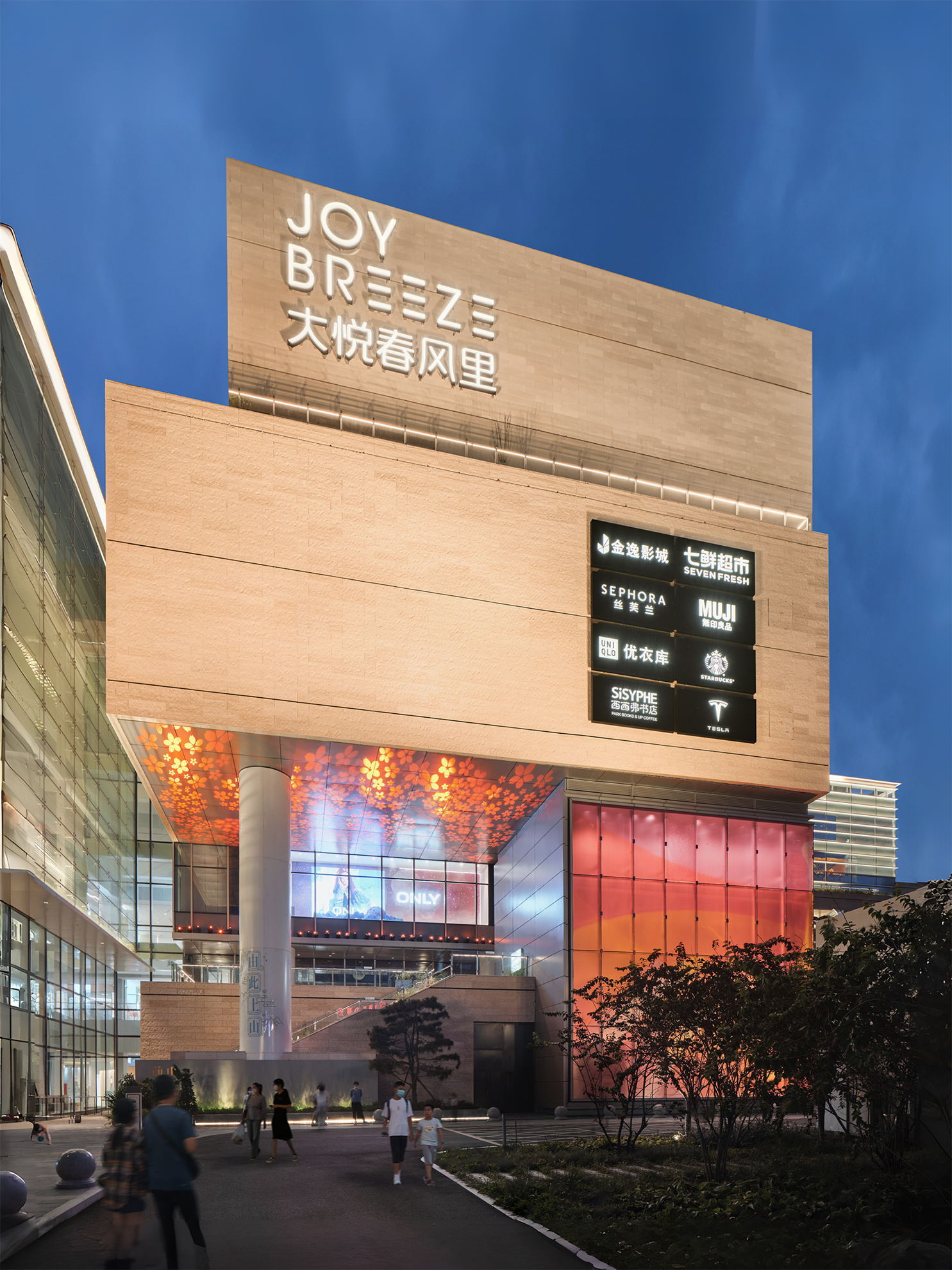 Sculptural entry to shopping center shows large stacked stone clad volumes supported by a large round column several stories up, 
                                                            a colorful glowing glass wall at its base, and a glowing glass wall on its left.