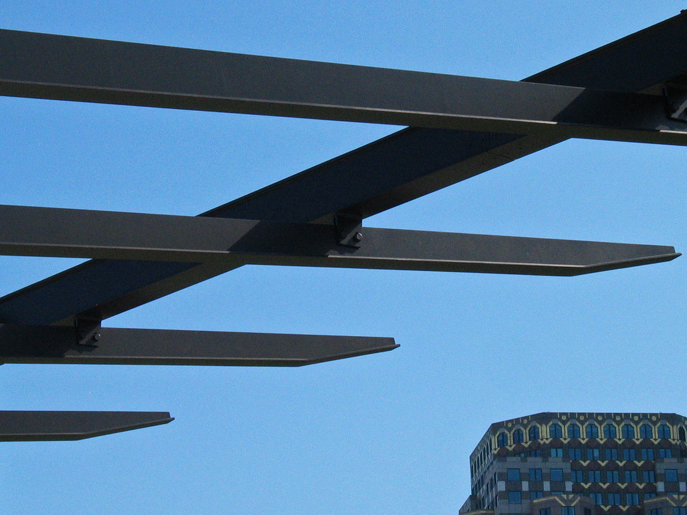 Close- up view of the ends of the dark brown steel purlins which project out into the park, which are tapered.