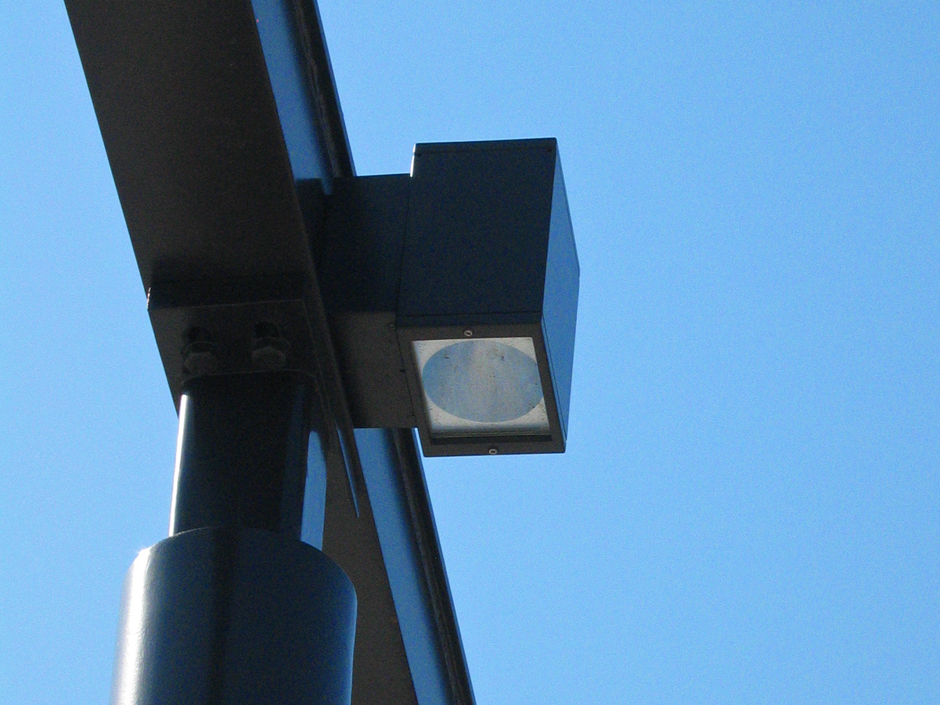 Close-up view of the downward projecting, rectangular dark brown light fixtures which are attached to the pergola beams.
