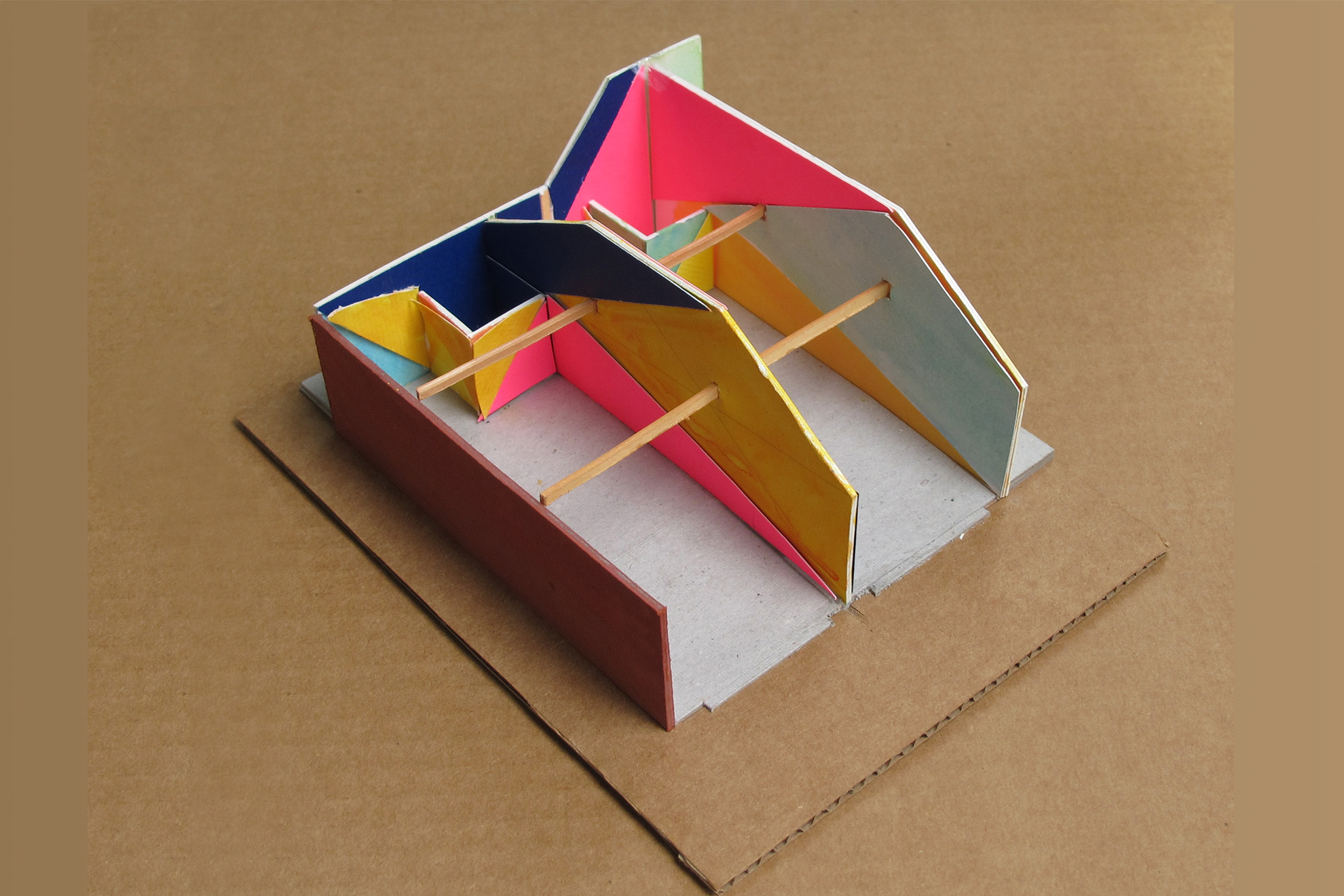 Colored carboard, paper, and wood model of the paint design of two workshop spaces, separated by a wall.
                The paint areas are cut diagonally &ndash; as are the forms of the ceiling (created by the angled roof) &ndash; 
                into large geometric shapes that span the entire length of the walls.