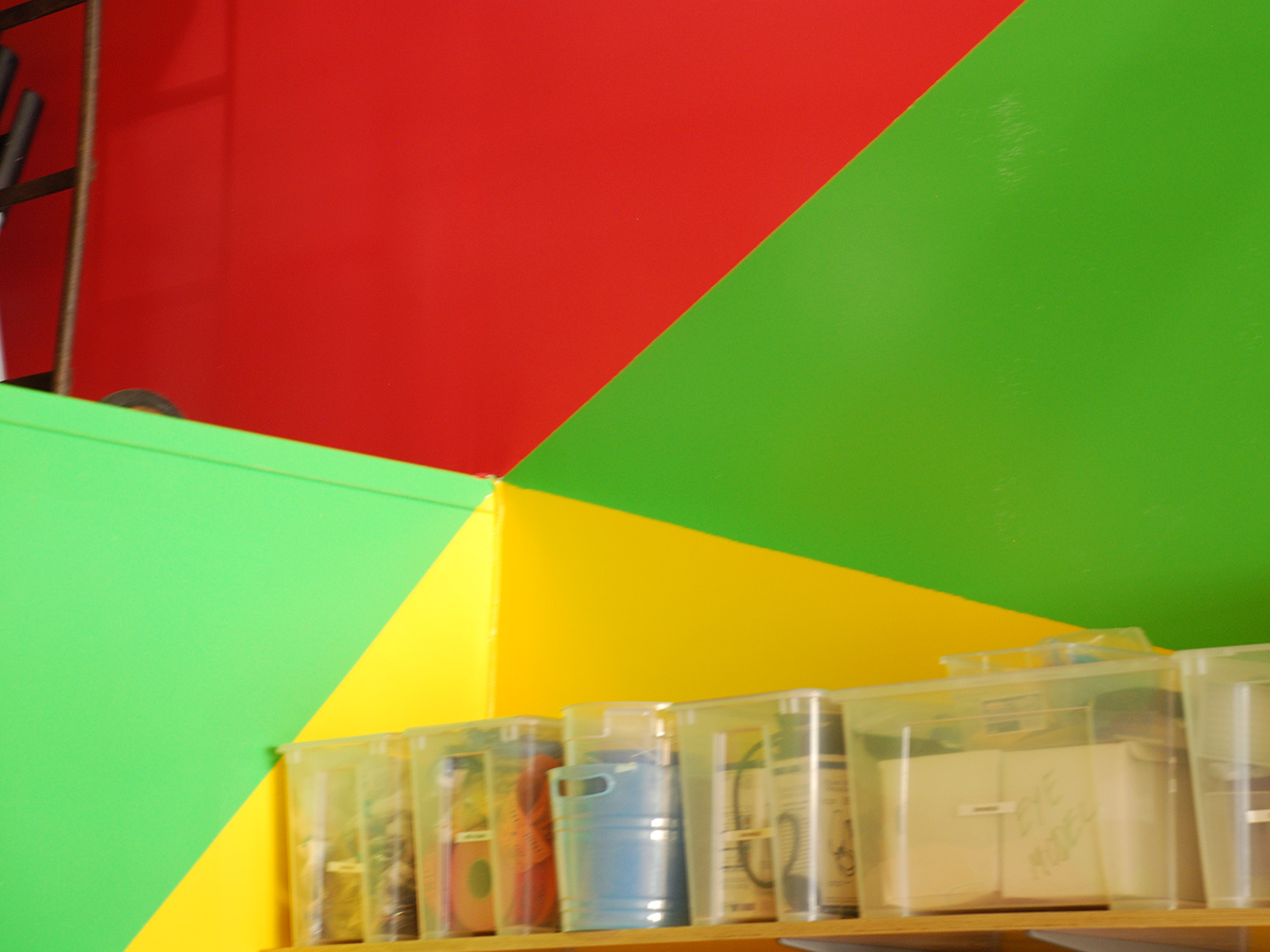 Zoom in on top corner of bathroom wall which pops out into the space showing triangular areas of yellow, green, and red paint coming to a point.