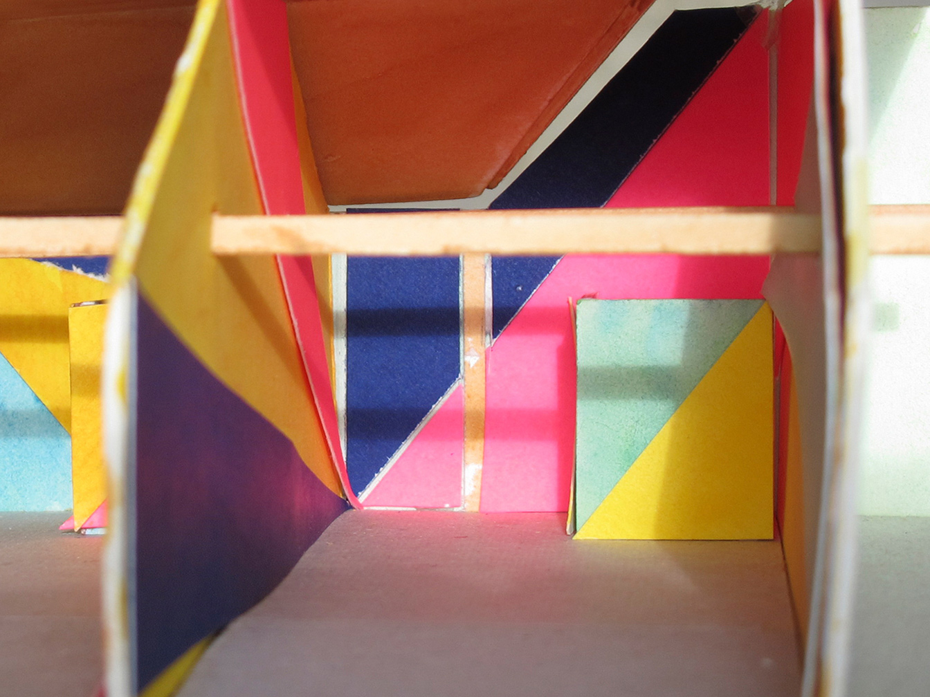 Zoom in on cardboard model of one workshop interior, with blue, yellow, and red triangular areas on the left wall, 
                                                                blue and red triangular areas on the back wall, and green and yellow triangular areas on a small wall with pops forward on the right.
