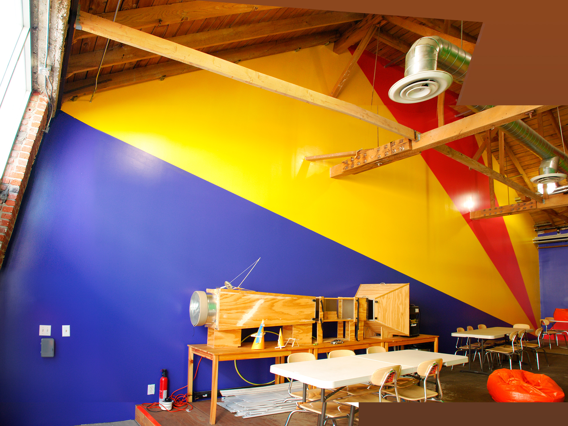 The left wall painted in large triangulated areas relating to the roof structure of blue at the bottom, 
                                                                    then yellow, then reddish-magenta, and yellow again, with part of the back wall showing painted blue.