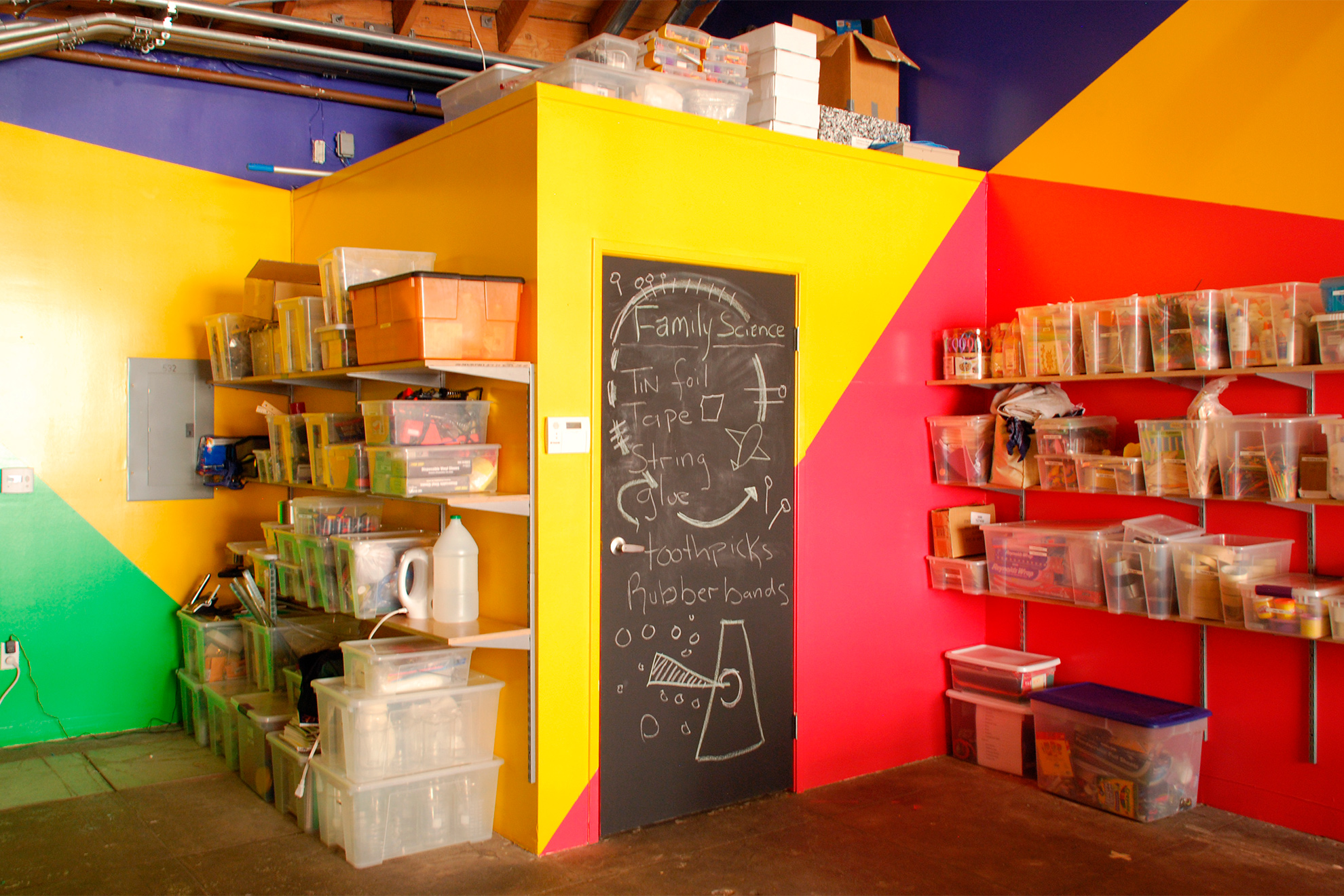 Zoom in on lower bathroom walls at the back of the space painted in triangulated break up of yellow and reddish-magenta, with the bathroom door painted with black chalk paint.